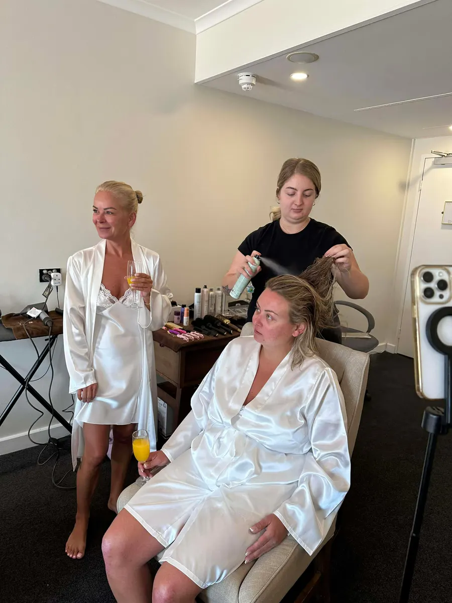 Bride and bridesmaid in robes having their hair styled on the morning of the wedding