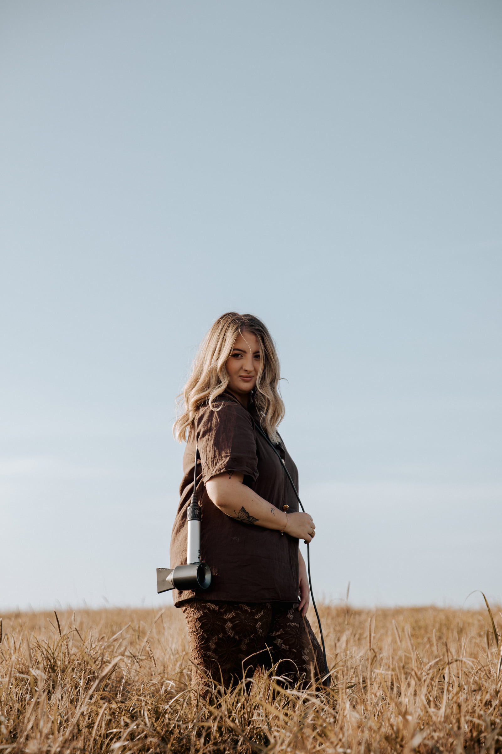 Kate Bonnie professional hairstylist with hairdryer standing in Pilbara grassland South Hedland